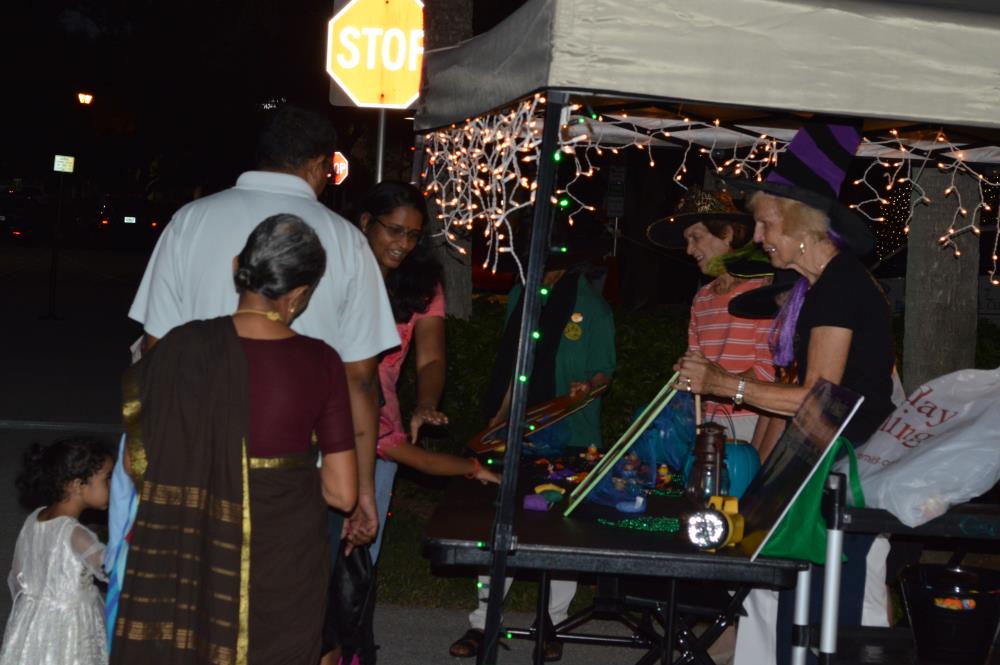 People look at street vendor items at a booth with woman dressed as witch behind it